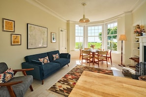 A living room with a blue sofa, a dining table with chairs, a fireplace, and large windows. - Kinclune House Buildings on Private Angus Estate (Kirriemuir)