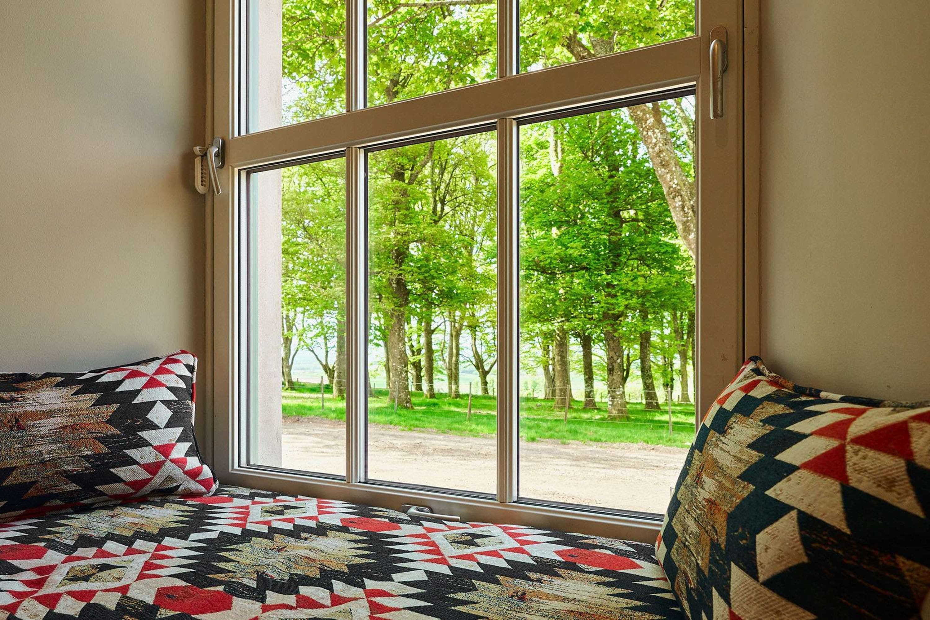 A room with a large window, two patterned cushions, and a view of a green landscape.