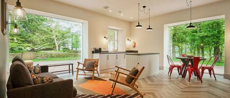 A spacious living area with a large window, a kitchen, and a dining area with red chairs.