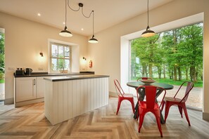 Una cocina moderna con una isla central, un comedor con sillas rojas y un amplio ventanal con vistas a un bosque.