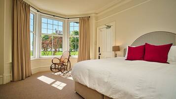 A bedroom with a large bed, a rocking chair, and a view of the outdoors through a bay window.