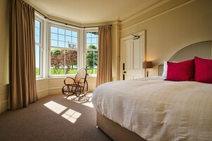 Un dormitorio con una cama grande, una silla, una ventana con cortinas y vistas a árboles.