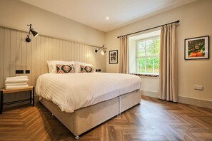 A bedroom with a large bed, a bedside table with towels, a window with curtains, and wall-mounted lights. - Barn Conversion at Kinclune Steading Angus Glens (Kirriemuir)