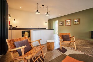 A modern kitchen with white cabinets, a black countertop, and a built-in oven. There are two wicker chairs with cushions, a round wooden stool, and a patterned rug on the floor. - Barn Conversion at Kinclune Steading Angus Glens (Kirriemuir)