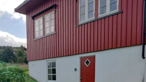 A red and white building with a door and windows, two wooden chairs, and a small table on a grassy area. - Apartment in Stamsund (Stamsund)