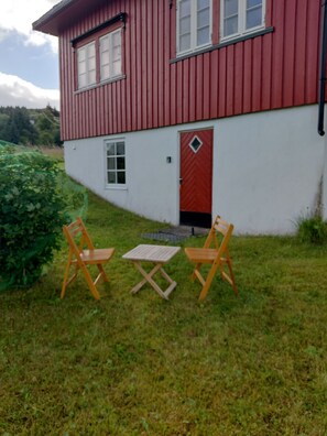 A red and white building with a door and windows, two wooden chairs, and a small table on a grassy area. - Apartment in Stamsund (Stamsund)