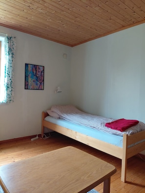 A single bed with a striped mattress, a wooden table, a wall-mounted light, and a painting on the wall. - Apartment in Stamsund (Stamsund)