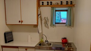 A compact kitchen with wooden cabinets, a sink, a stove, and a window with curtains. - Apartment in Stamsund (Stamsund)