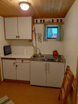 A compact kitchen with wooden cabinets, a sink, a stove, and a window with curtains. - Apartment in Stamsund (Stamsund)