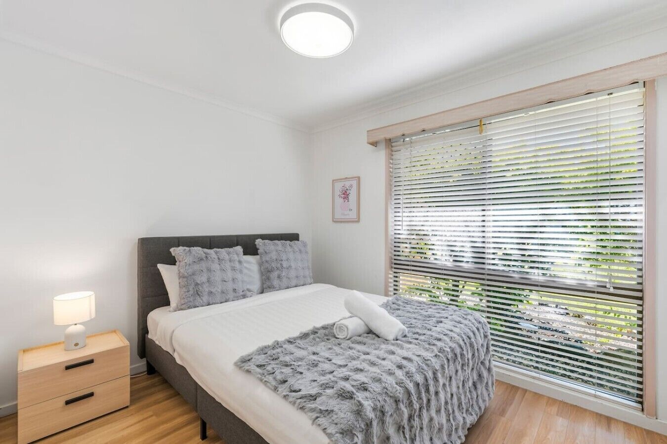 A bedroom with a bed, bedside table, lamp, and window with blinds.