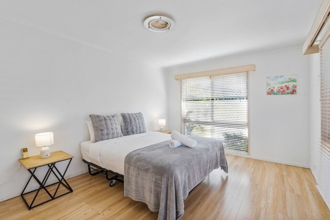 A bedroom with a bed, bedside table, lamp, and a window with blinds.