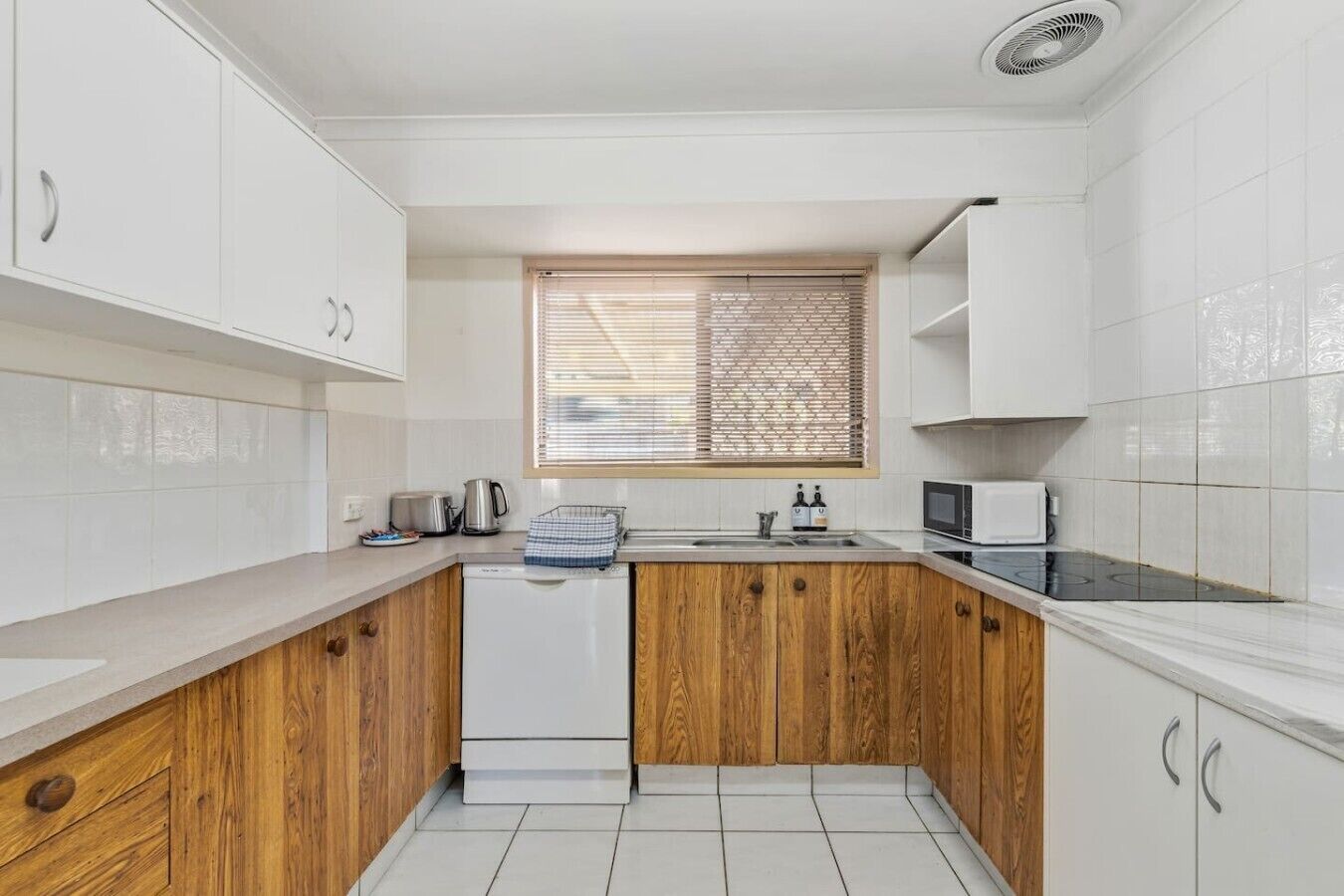 A kitchen with white cabinets, a wooden countertop, a dishwasher, a stove, and a window with blinds.