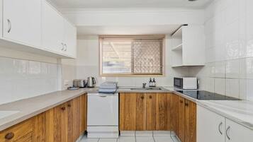 A kitchen with white cabinets, a wooden countertop, a dishwasher, a stove, and a window with blinds.