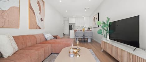 A modern living room with a sofa, a coffee table, a TV, and a dining area in the background.