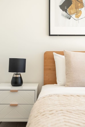 A neatly arranged bedroom with a bed, a bedside table with a lamp, and a framed picture on the wall. - Brand-New Premium Retreat|Pool &Gym| Parking|Train (Mitchelton)
