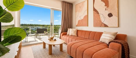 A modern living room with a sofa, a coffee table, and a large window offering a view of the outdoors.