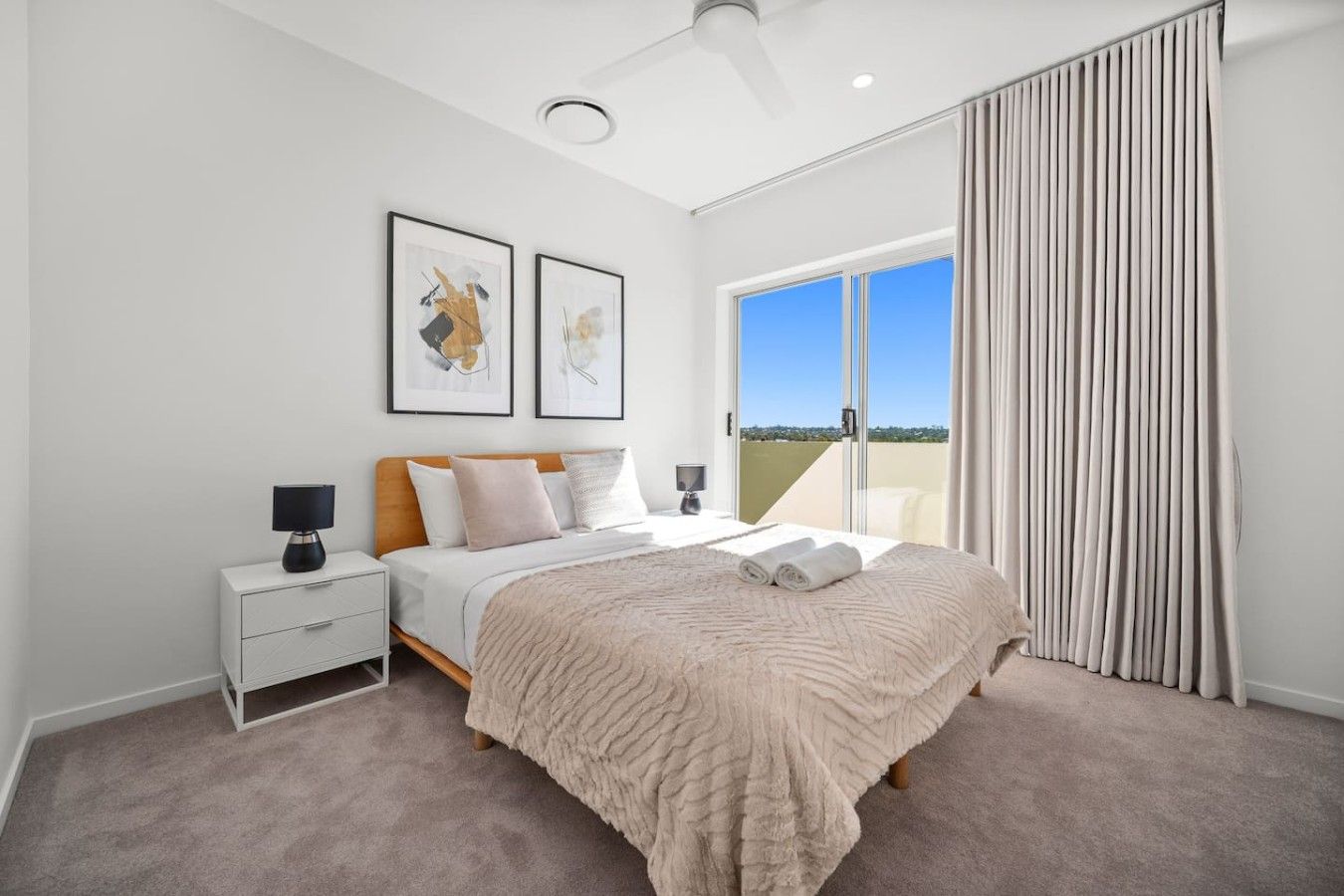 A bedroom with a bed, nightstands, a ceiling fan, and a large window with curtains.