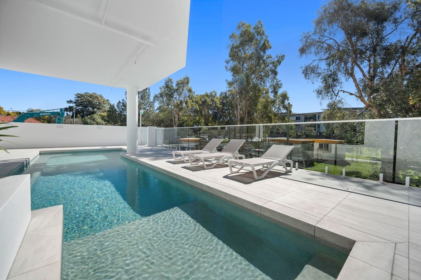 Una piscina con agua cristalina, rodeada por una terraza blanca y sillones de descanso.