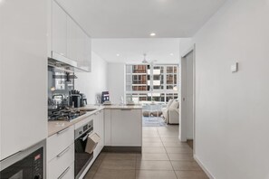 A modern kitchen with white cabinetry, a central island, and a dining area with a sofa. - The Valley Great Value| Sofa Bed |Parking|Pool&Gym (Fortitude Valley)