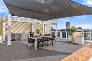 Eine Terrasse im Freien mit Tisch, Stühlen, einem Grill und Kübelpflanzen.