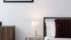 A bedroom with a bed, a bedside table with a lamp, a wooden cabinet, and a framed artwork on the wall. - The Valley Great Value| Sofa Bed |Parking|Pool&Gym (Fortitude Valley)