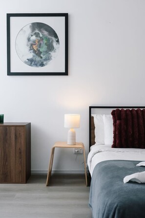 Ein Schlafzimmer mit einem Bett, einem Nachttisch mit Lampe, einem Holzschrank und einem gerahmten Kunstwerk an der Wand.