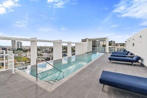Et rooftop-infinity pool med krystalklart udsyn over bybilledet, omgivet af moderne arkitektur og møbleret med liggestole.