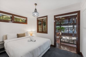 A bedroom with a bed, bedside lamp, and a view of an outdoor seating area through a glass door. - Family-Friendly Stay | 2 Living + Ducted Aircon (Graceville)