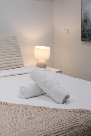 Ein ordentlich bezogenes Bett mit aufgerollten Handtüchern und einer Nachttischlampe.
