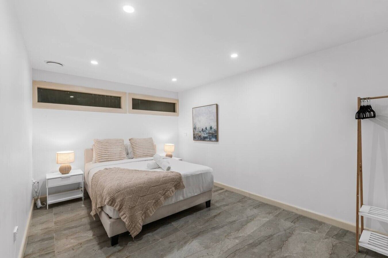 A bedroom with a bed, bedside tables, a window, and a coat rack.