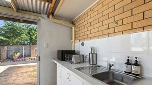 Eine Küche mit Backsteinwand, weißen Schränken, einer Spüle aus Edelstahl und einem Fenster mit Blick auf einen Garten.