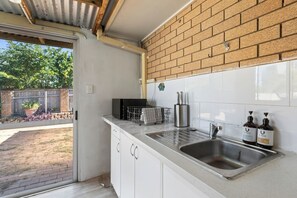 Eine Küche mit Backsteinwand, weißen Schränken, einer Spüle aus Edelstahl und einem Fenster mit Blick auf einen Garten.