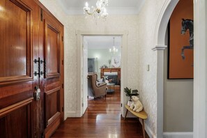 A hallway with wooden doors, a chandelier, and a dining area in the background.