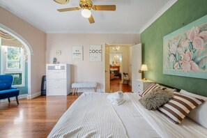 A bedroom with a bed, a desk, a chair, and a painting on the wall.