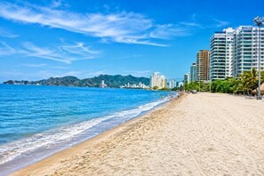 A beach with a clear blue sky, a sandy shore, and a cityscape with high-rise buildings in the background. - Modern apartment for rent in Pozos Colorados, Santa Marta (Santa Marta)