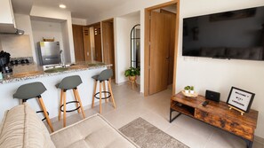 A modern living room with a sofa, three bar stools, a wooden coffee table, a flat-screen TV, and a welcome sign. - Modern apartment for rent in Pozos Colorados, Santa Marta (Santa Marta)