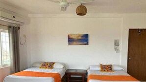 A room with two wooden beds, a small table, a ceiling fan, and a painting on the wall. - Casa MIrador Hotel & Surf Camp (Salina Cruz)