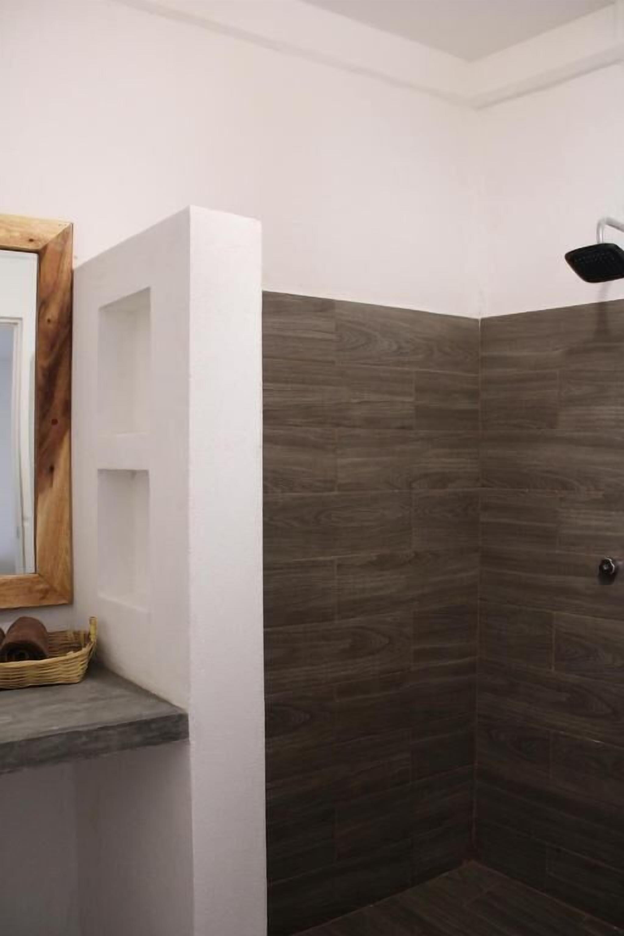 A shower area with dark wooden tiles, a white wall, and a wooden-framed mirror.