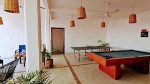 A pool table in a room with a ceiling fan, hanging wicker lamps, and a small seating area with a chair and a table. - Casa MIrador Hotel & Surf Camp (Salina Cruz)