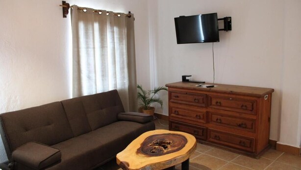 A living room with a brown sofa, a wooden coffee table, a wooden dresser, and a television mounted on the wall. - Casa MIrador Hotel & Surf Camp (Salina Cruz)