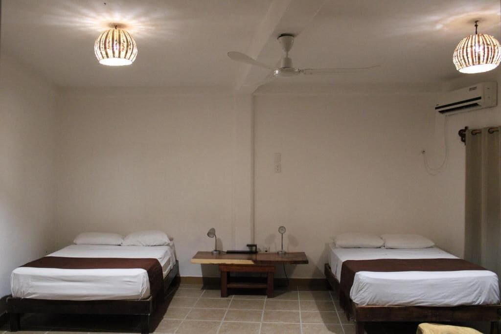 A room with two single beds, a ceiling fan, and two pendant lights.