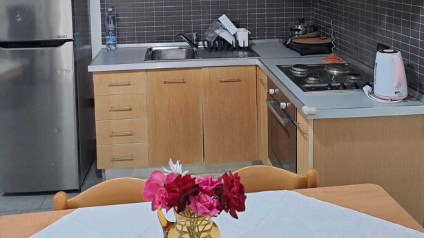 Eine moderne Küche mit Holzschränken, einem Edelstahlkühlschrank, einer Spüle und einem Esstisch mit Blumen in einer Vase.
