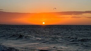 Un coucher de soleil sur l’océan, avec un ciel dégagé et un seul cerf-volant dansant dans les airs.