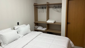 Une chambre à coucher avec un lit, une armoire en bois où sont suspendus des vêtements, et une porte.