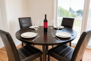 Ein runder Esstisch mit vier Stühlen, einer Weinflasche und leeren Weingläsern.
