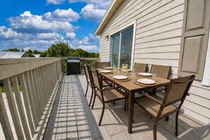 Eine Terrasse im Freien mit Esstisch für vier Personen, einem Grill und einer Terrassentür zu einem Haus.