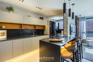 Uma cozinha moderna com ilha central, banquetas e iluminação pendente.
