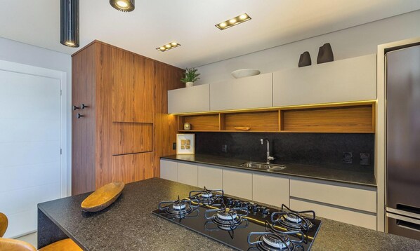 A modern kitchen with a central island, built-in cabinets, and a stainless steel refrigerator. - Sophisticated Apt Near Covered Street Dlh0403 (Gramado)