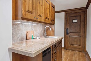 Eine Küche mit Holzschränken, einer Granit-Arbeitsplatte, einem Edelstahl-Spülbecken und einer Holztür.