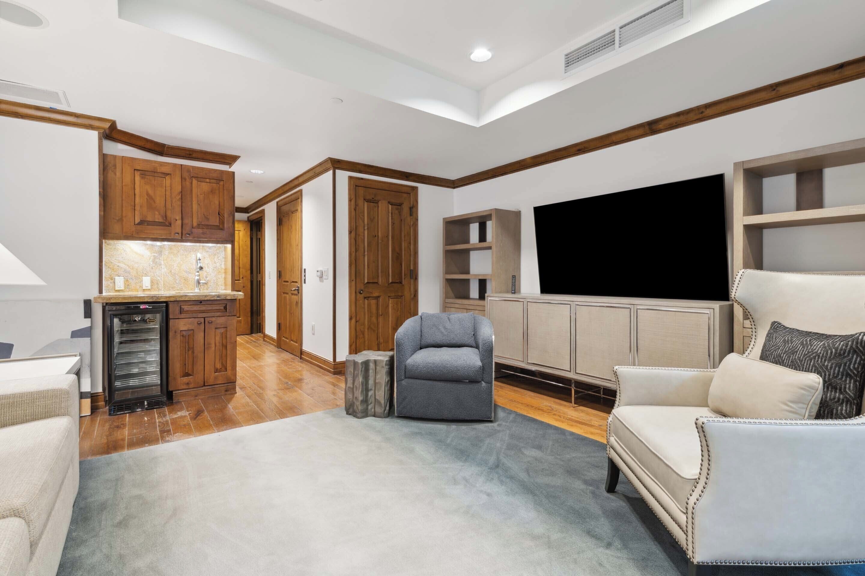 Un salón amplio con un sillón gris, un sofá blanco y un televisor de pantalla plana montado en la pared.